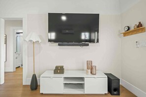 Ein modernes Wohnzimmer mit flachbildfernseher an der Wand, einer weißen Unterhaltungsanlage mit Stauraum, einer Stehlampe und einem kleinen Regal mit Dekoration.