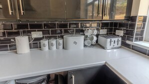 Una cocina con salpicadero de azulejos negros, armarios de acero inoxidable, encimera blanca y un tostador.