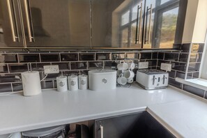 Keittiössä on mustat laatat välitilassa, ruostumattomasta teräksestä valmistetut kaapit, valkoinen työtaso ja leivänpaahdin.
