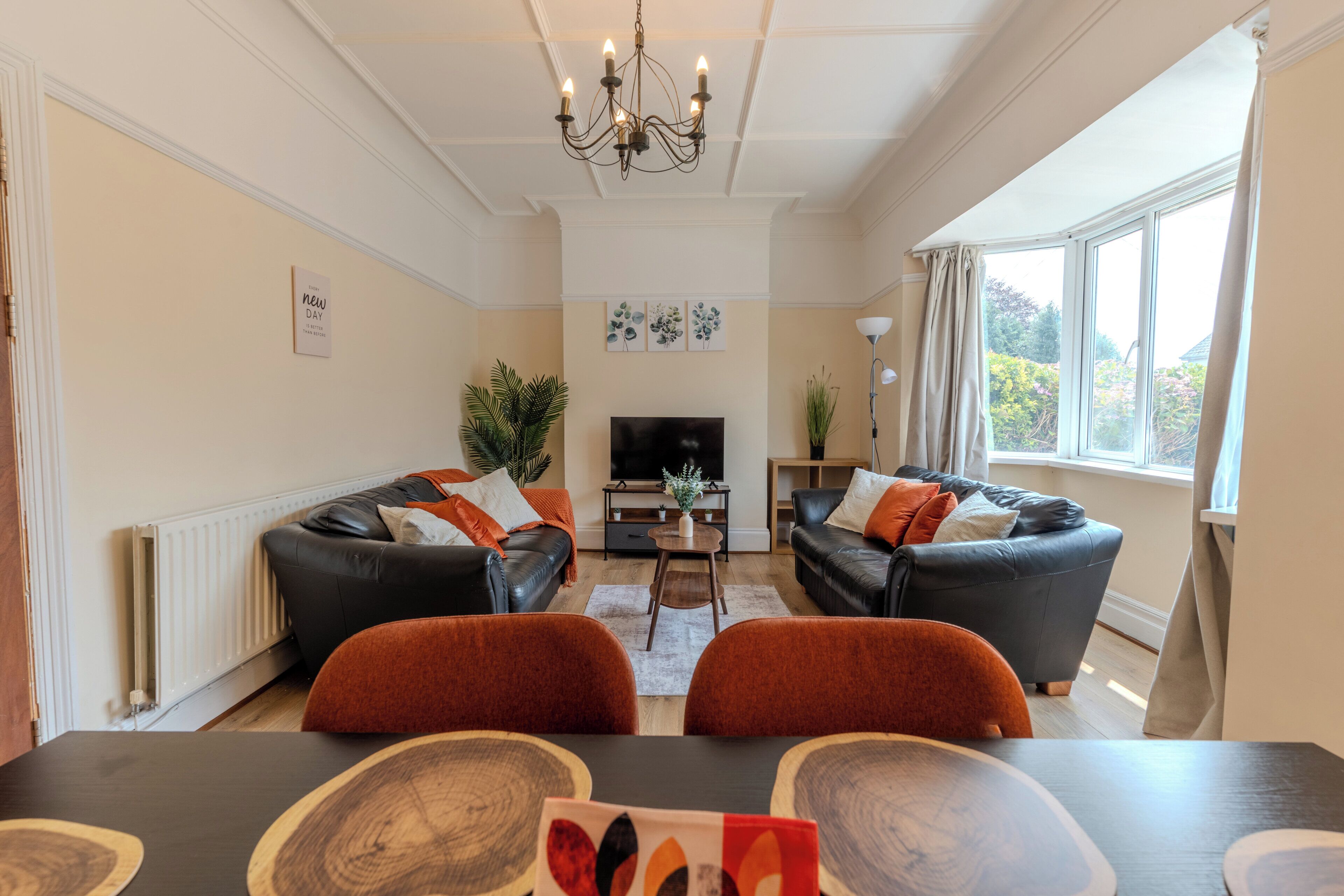 Een woonkamer met twee banken, een televisie, een kroonluchter en een eettafel met stoelen.