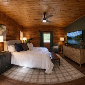 A bedroom with a bed, bedside tables, a chair, a dresser, a ceiling fan, and a TV mounted on the wall. - Hocking Hills, Pool, Hottub & Sauna (Logan)