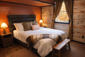A wooden-paneled bedroom with a bed, bedside lamps, a bench, and a window with curtains. - Hocking Hills, Pool, Hottub & Sauna (Logan)