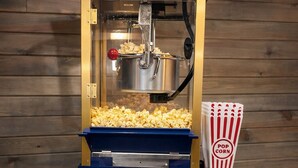 En popcornmaskine i vintage-stil med en blå base og guld detaljer, med en klar beholder til popcorn og en rød knap.