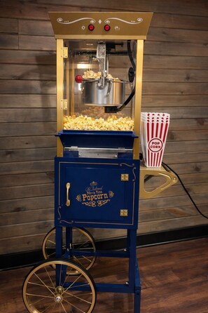 Eine Popcornmaschine im Vintage-Stil mit blauer Basis und goldenen Akzenten, ausgestattet mit einem transparenten Behälter für Popcorn und einem roten Knopf.