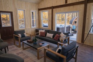 A cozy cabin interior with a sofa set, coffee table, and large windows offering a view of the outside. - Hocking Hills, Pool, Hottub & Sauna (Logan)
