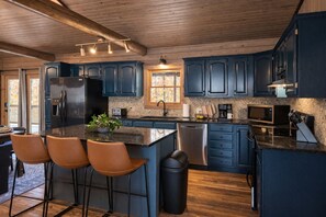 A modern kitchen with dark blue cabinets, a stainless steel refrigerator, a built-in microwave, and a large island with bar stools. - Hocking Hills, Pool, Hottub & Sauna (Logan)