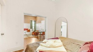 A room with a bed, a desk, and a chair. There is a door leading to another room.