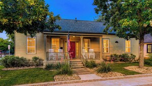 A two-story house with a front porch, a red door, and an American flag.