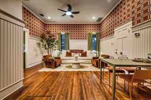 Una habitación con pared de ladrillo estampado, ventilador de techo, sofá, mesa de centro y mesa de comedor con sillas.