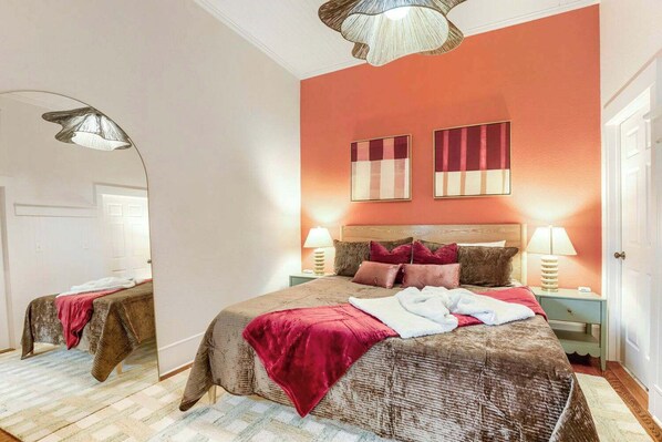 A bedroom with a large bed, two bedside tables, a mirror, and a ceiling light fixture.