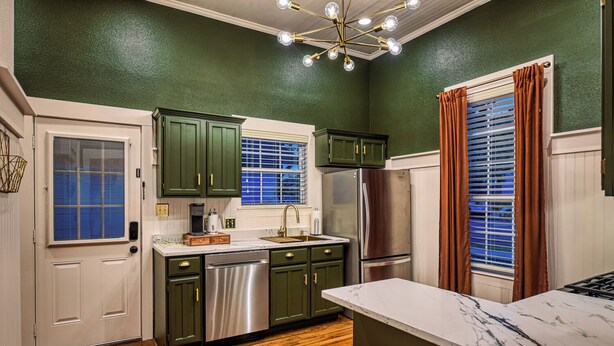 A kitchen with green cabinets, stainless steel appliances, a marble countertop, and a wooden bench.