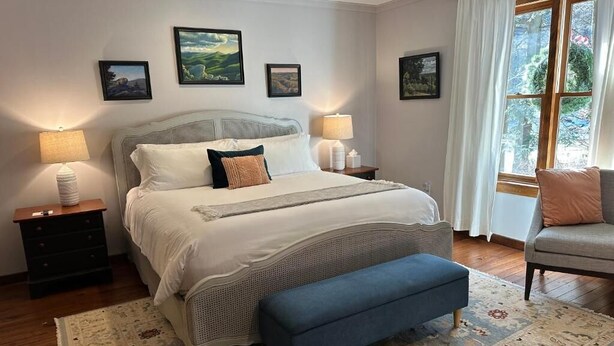 A bedroom with a bed, bedside tables, a bench, and a window with curtains.