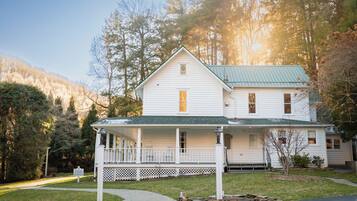 A two-story white house with a green roof, a covered porch, and a stone foundation.