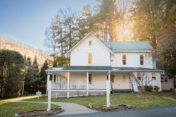 A two-story white house with a green roof, a covered porch, and a stone foundation. - Lovill House Inn (Boone)