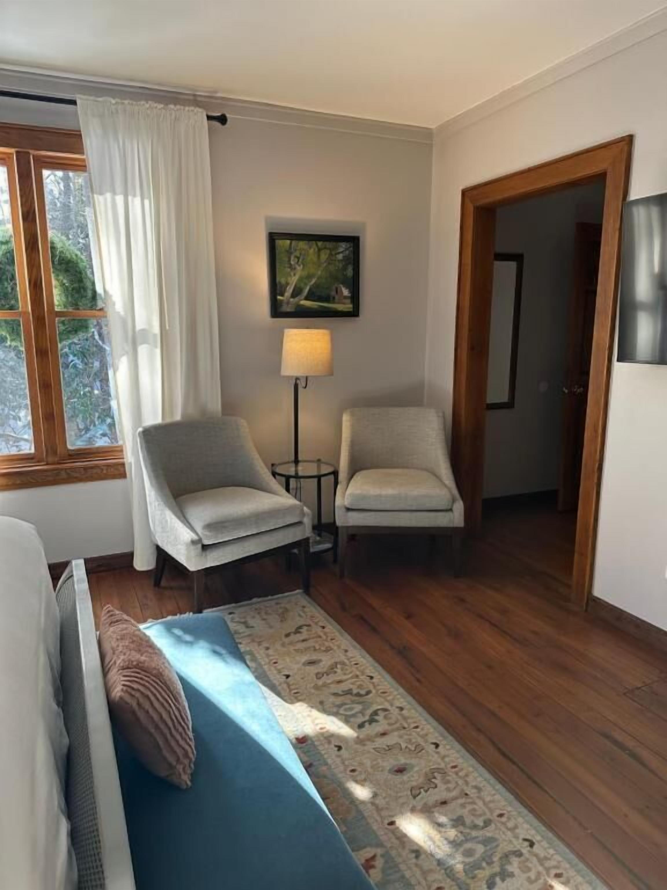 A room with a bed, two chairs, a lamp, a rug, and a painting on the wall.