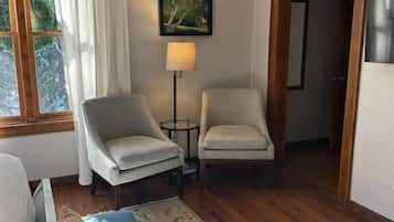 A room with a bed, two chairs, a lamp, a rug, and a painting on the wall.