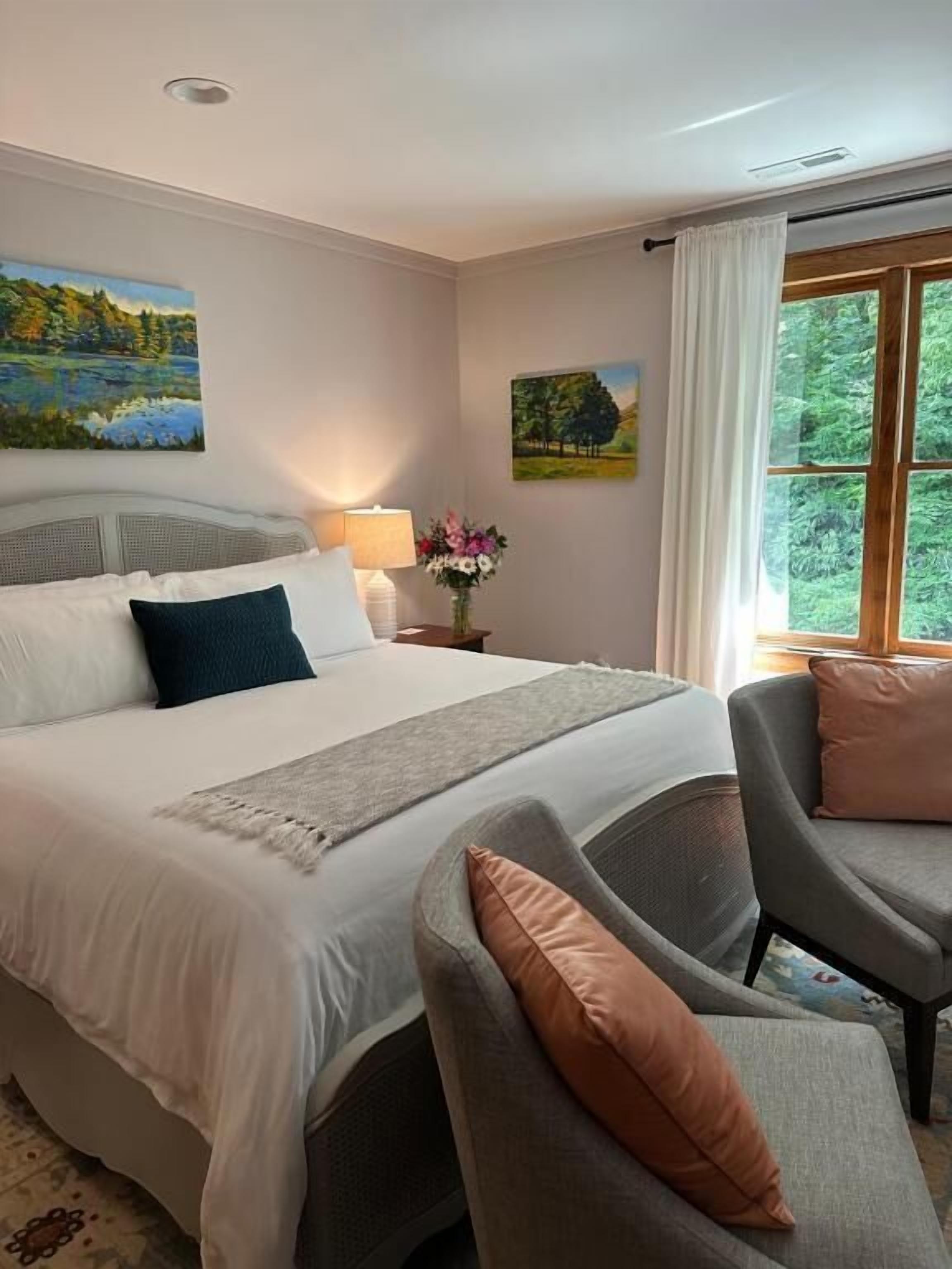 Ein Hotelzimmer mit einem großen Bett, einer Sitzecke mit einem Sessel, einem Nachttisch mit Lampe und einem Fenster mit Vorhängen.