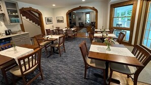 A dining area with multiple tables and chairs, a staircase, and a view through large windows.