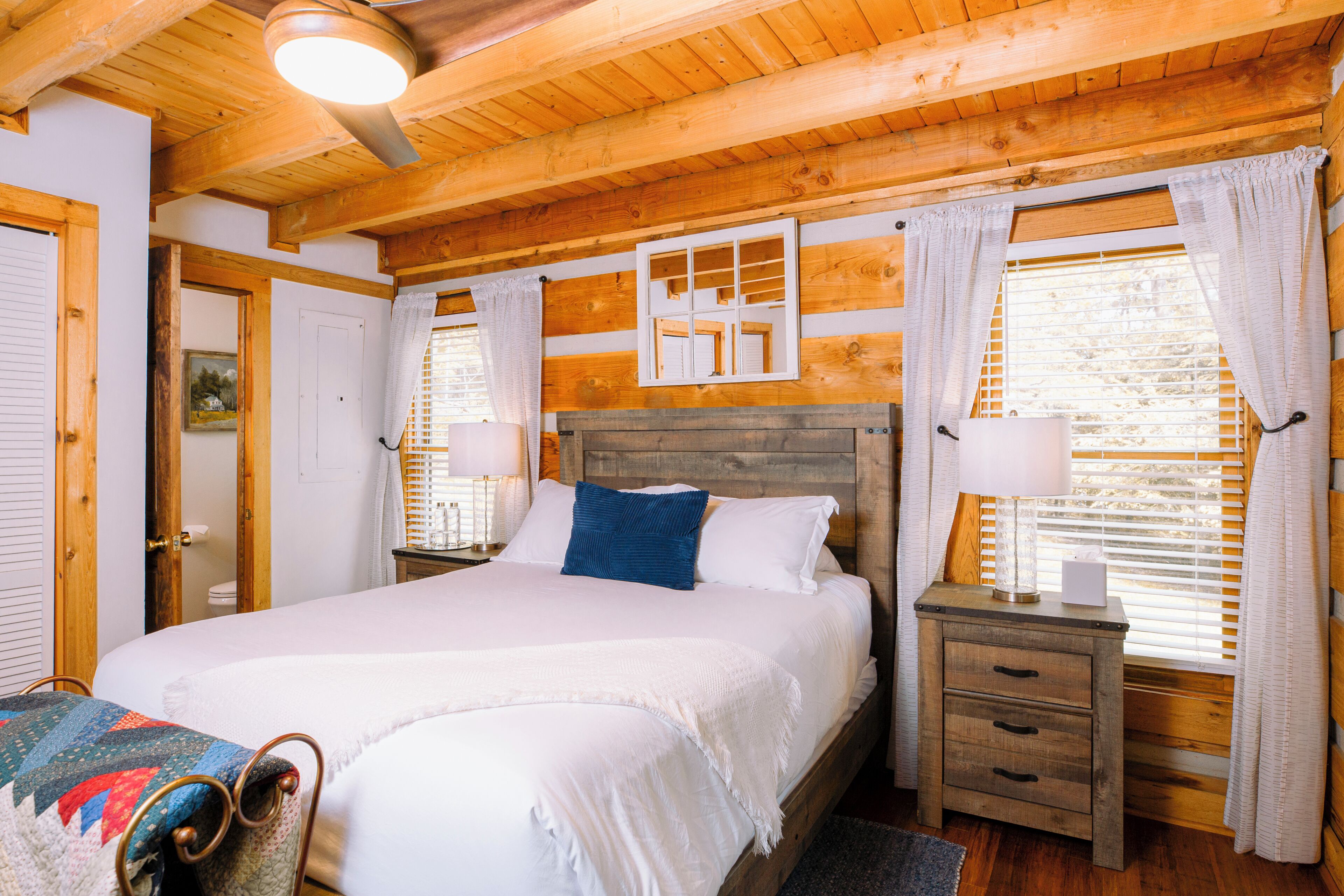 Un dormitorio con paneles de madera, una cama grande, mesitas de noche y una ventana con cortinas.