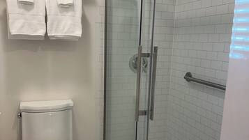 A bathroom with a glass-enclosed shower, a toilet, and a shelf with folded towels.