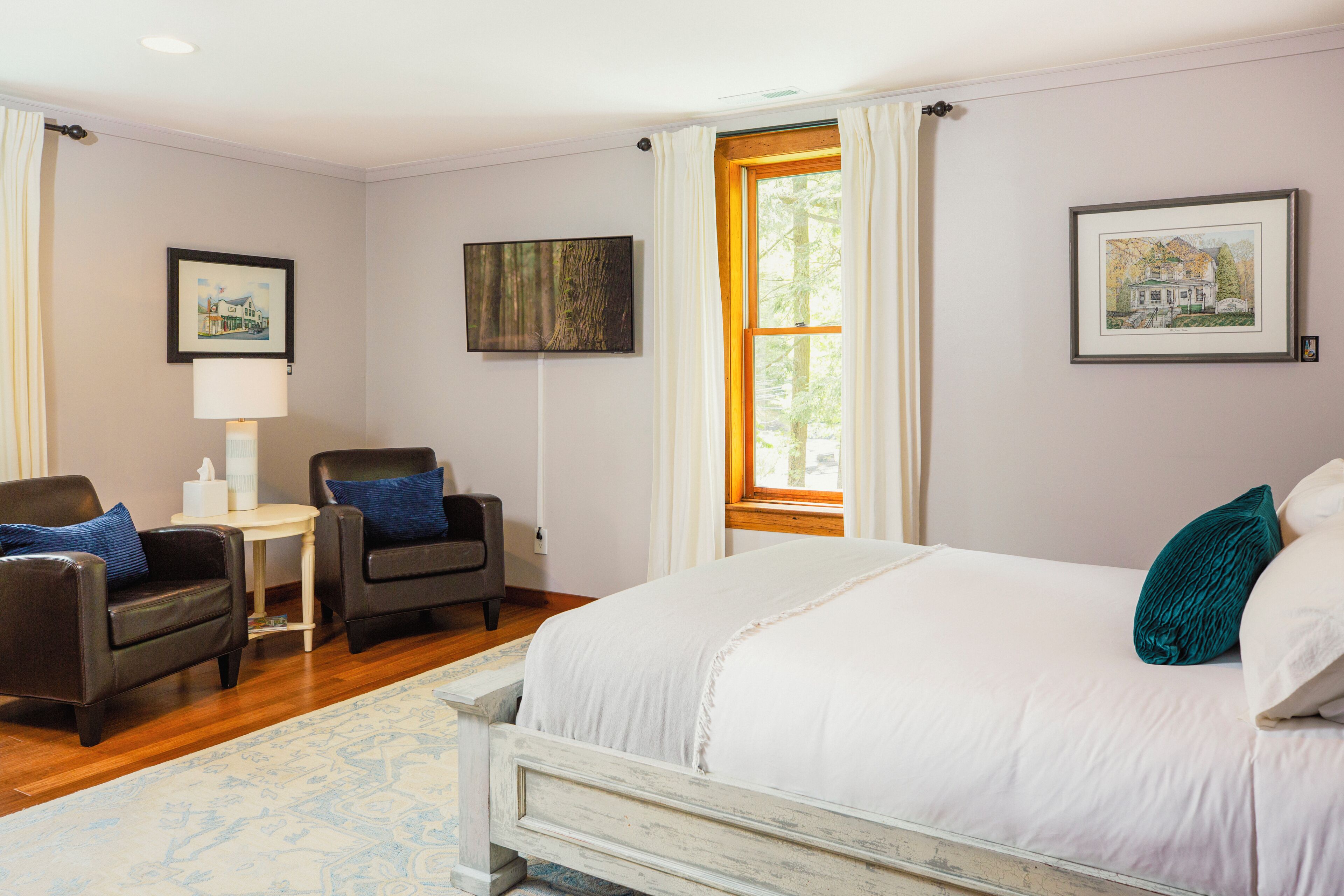 Habitación de hotel con cama, dos sillones, una mesita, lámpara y obras de arte en las paredes.