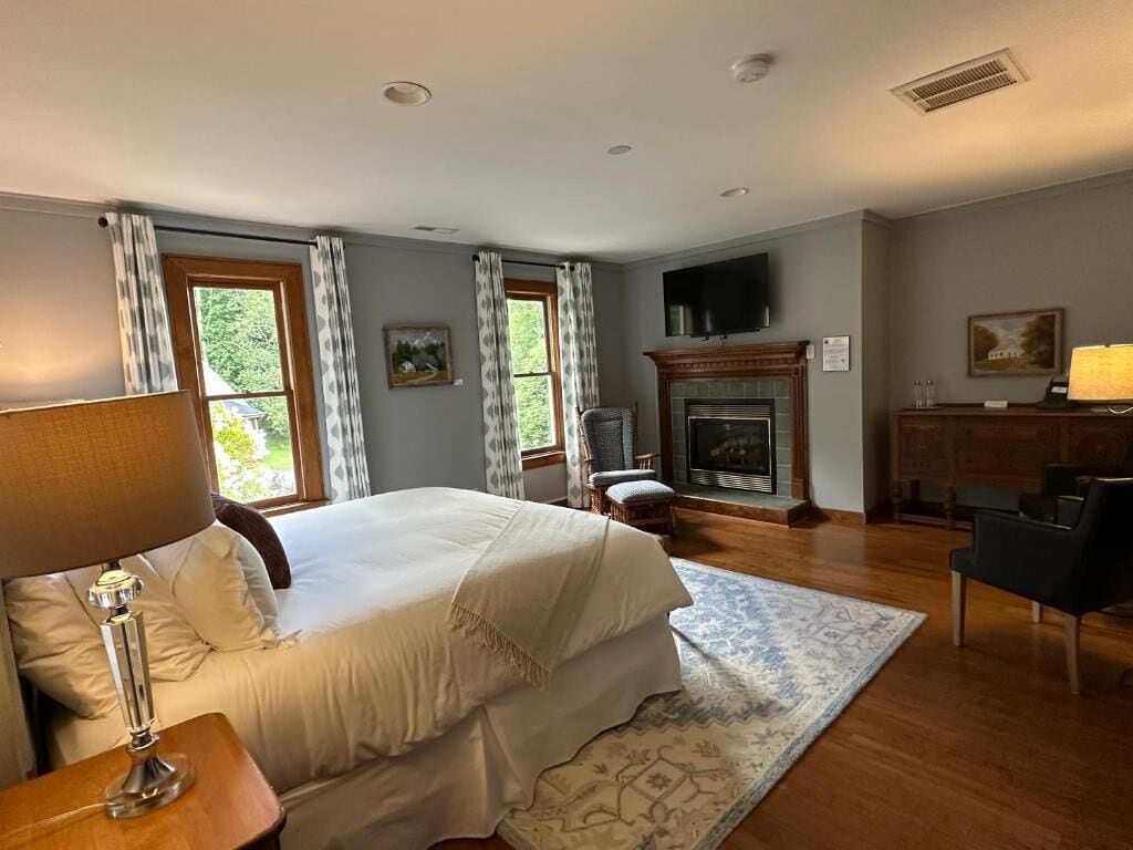 Un dormitorio con cama, chimenea, televisor y escritorio con lámpara.