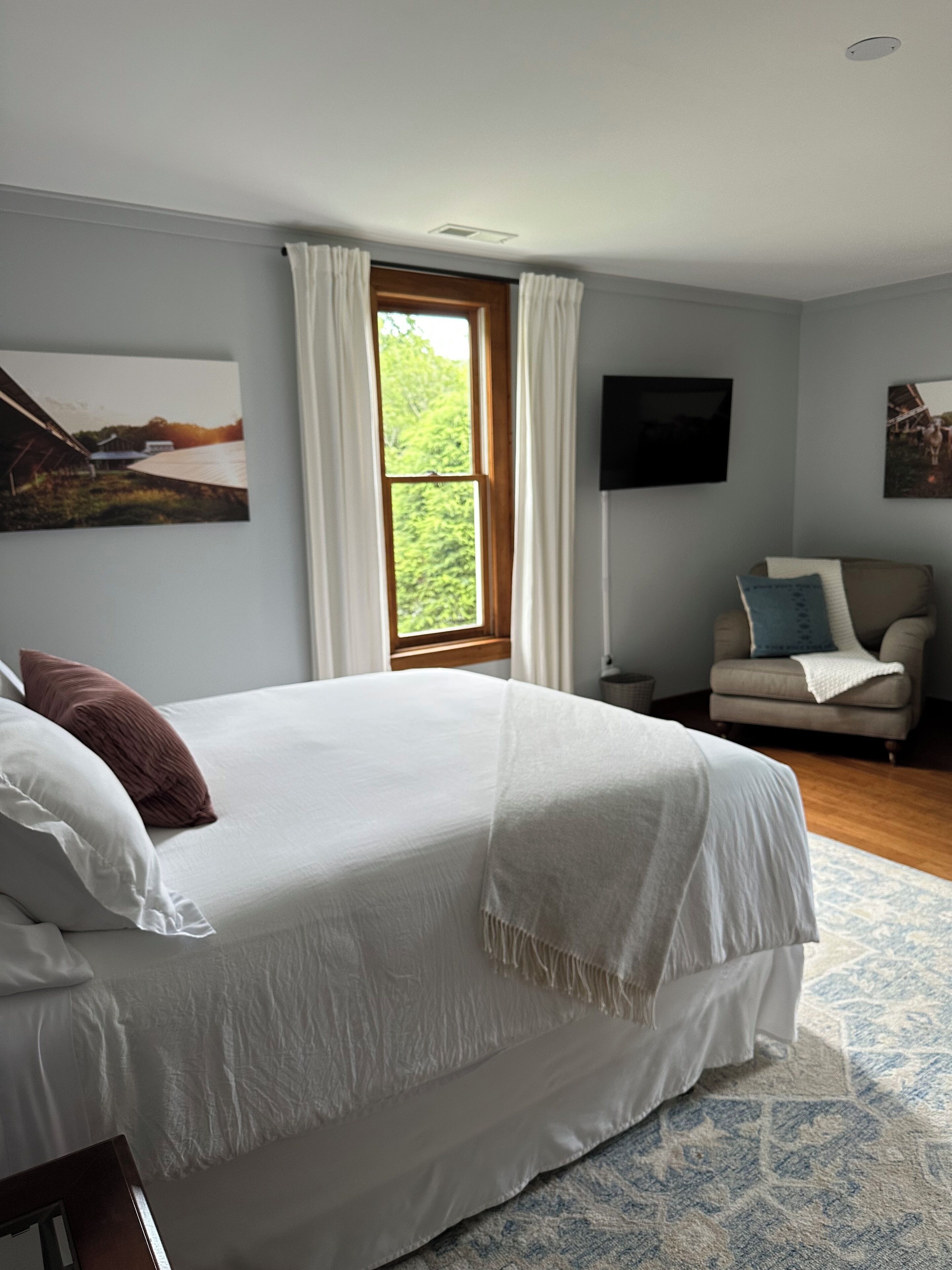 A bedroom with a large bed, a window, a sofa, and a flat-screen TV.