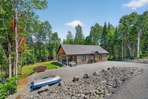 A cabin with a porch, a covered outdoor seating area, and a boat in the foreground.