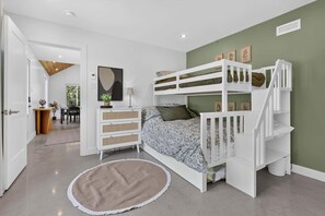 A child's bunk bed with a desk and chair, a round rug, and a painting on the wall.