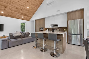 A modern kitchen with a central island, bar stools, a built-in oven, and a stainless steel refrigerator.