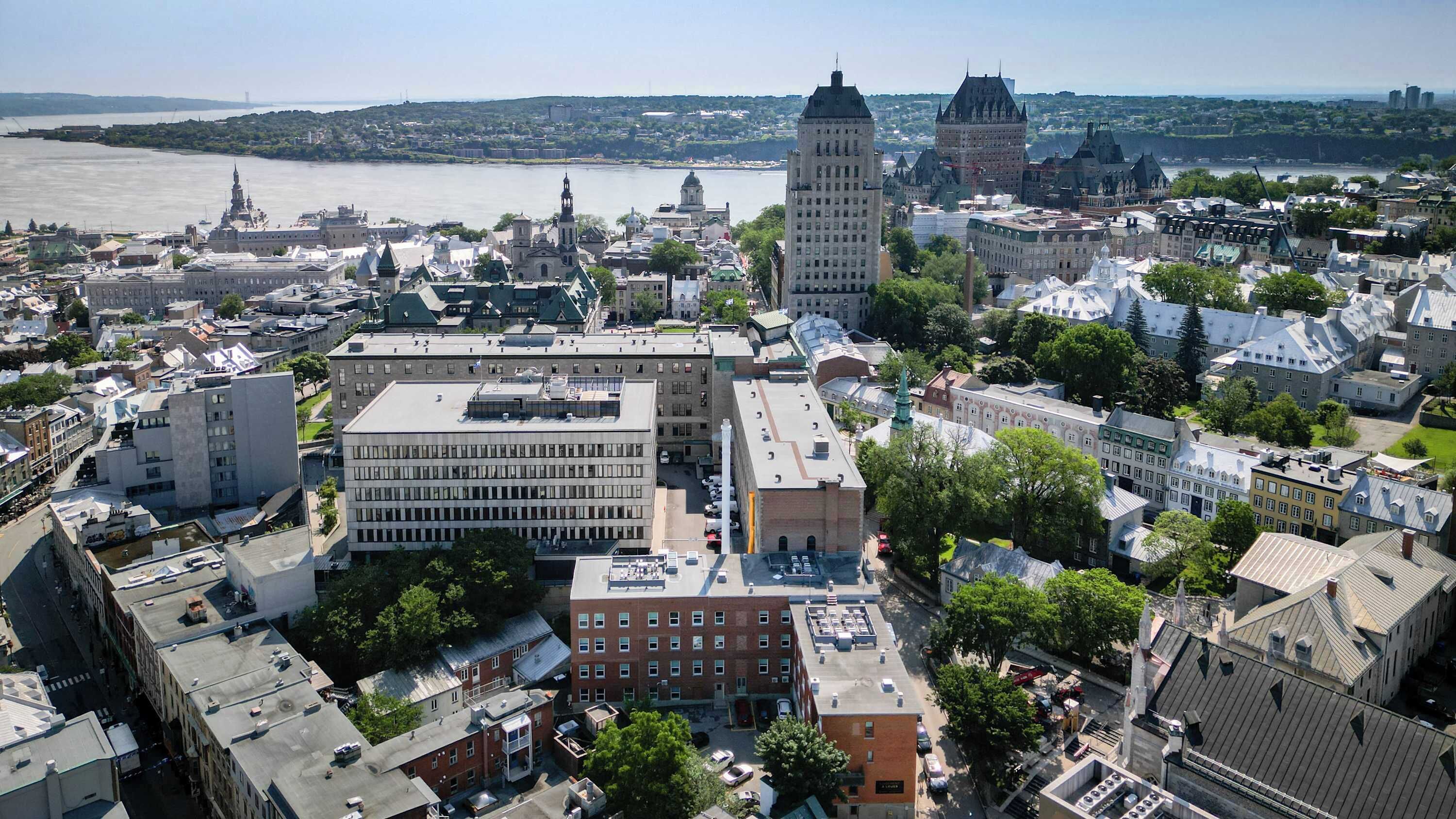 An aerial view of a cityscape with various buildings, including a prominent tower and a river in the background.