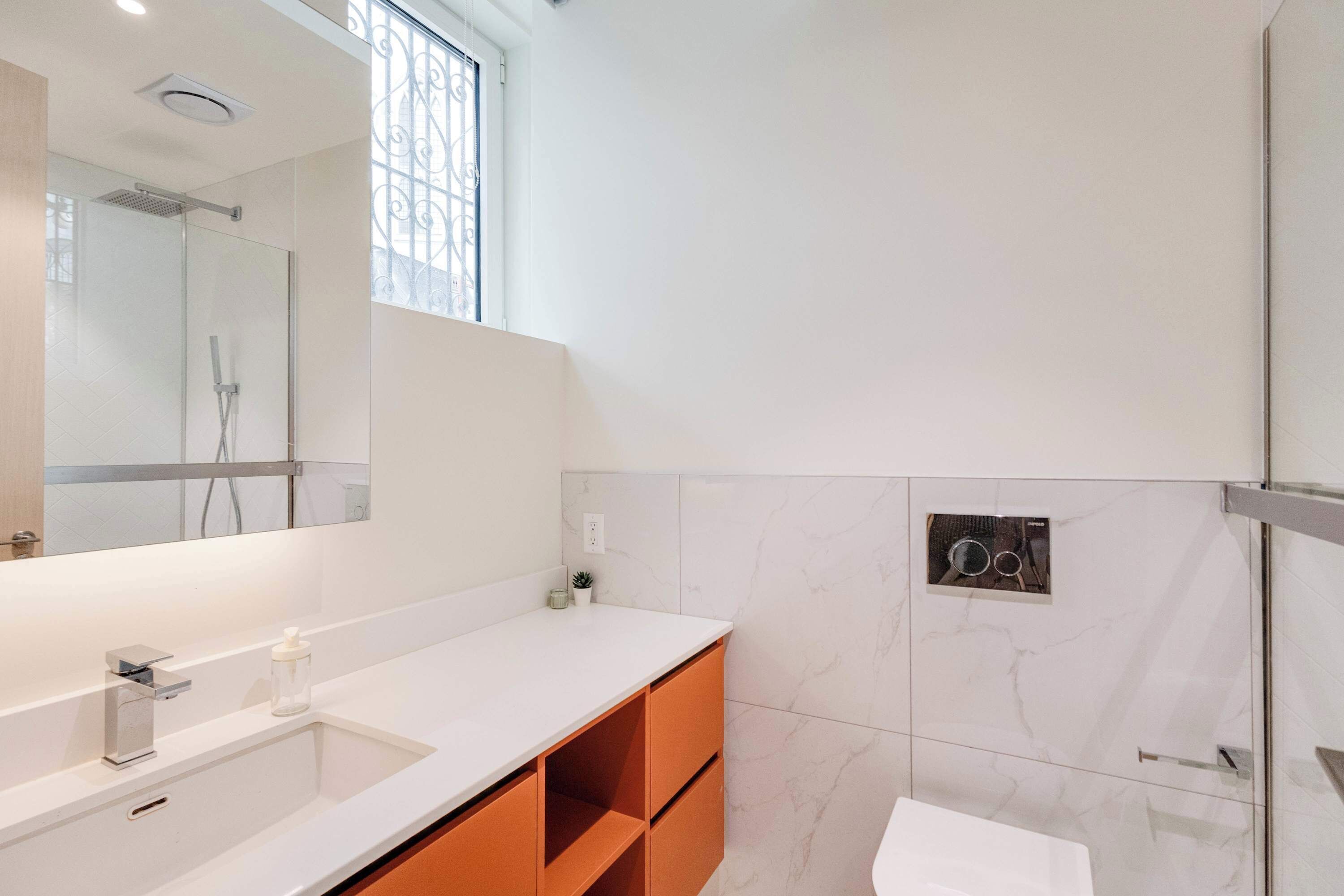 A modern bathroom with a large mirror, a white sink, and a shower area.