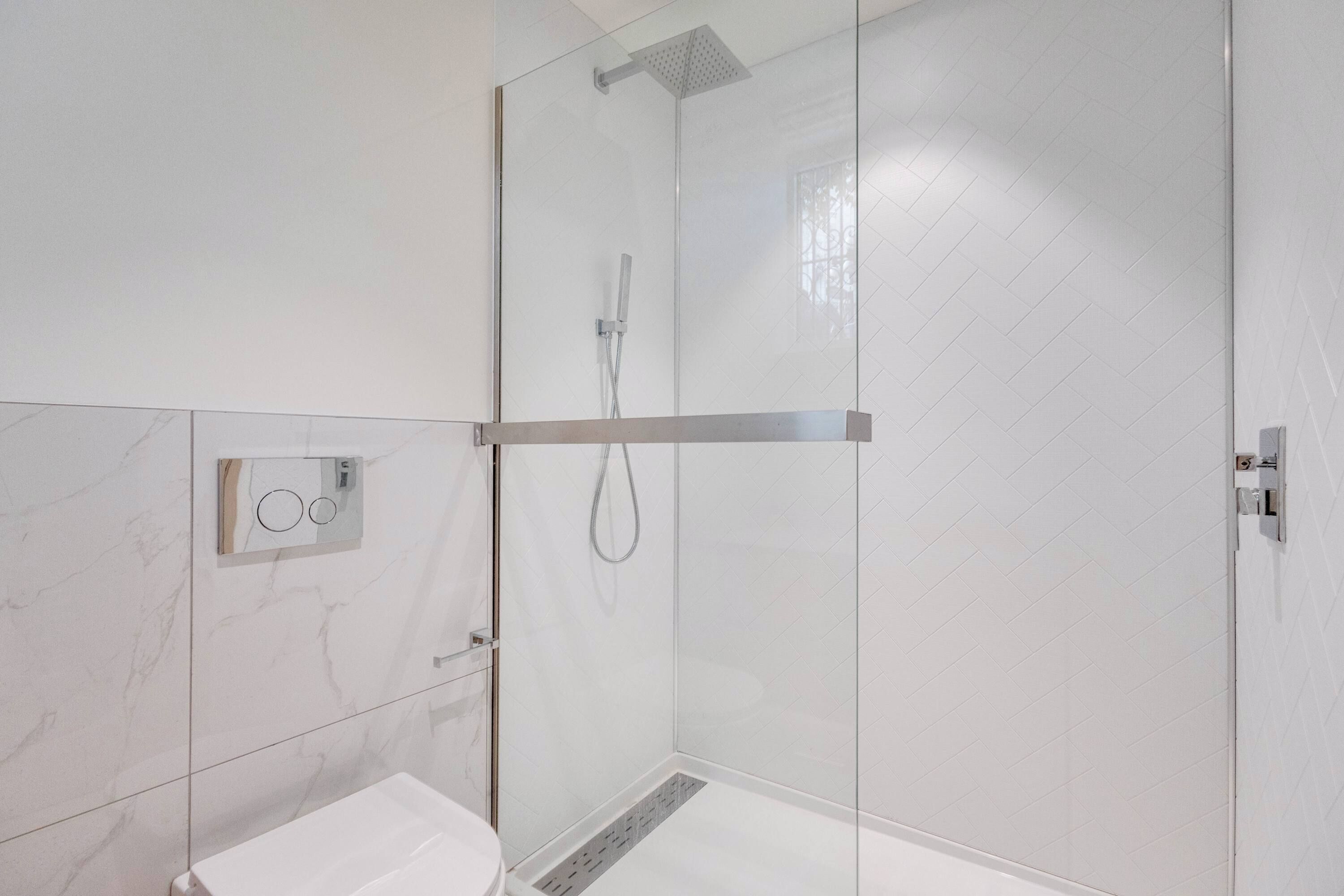 A modern bathroom with a glass-enclosed shower, a toilet, and a control panel.