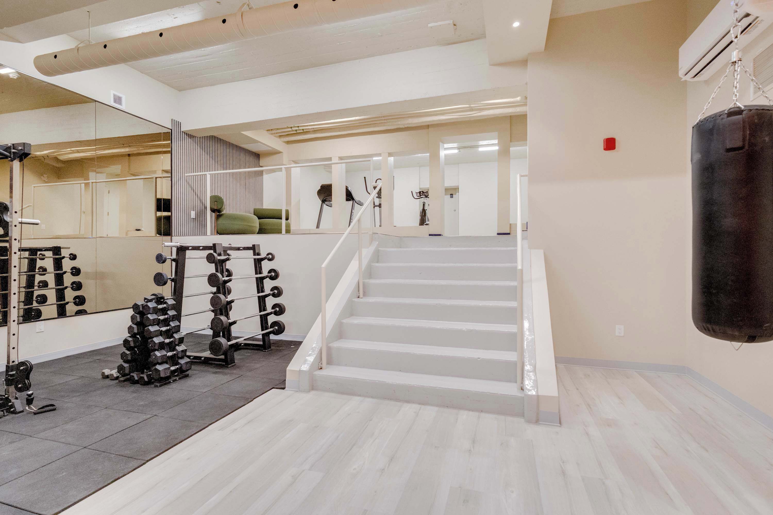 A gym with a staircase, weightlifting equipment, and a punching bag.