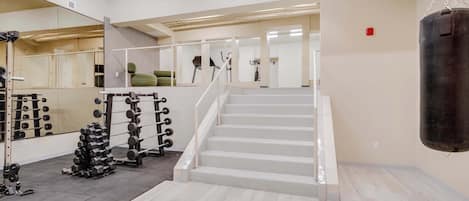 A gym with a staircase, weightlifting equipment, and a punching bag.