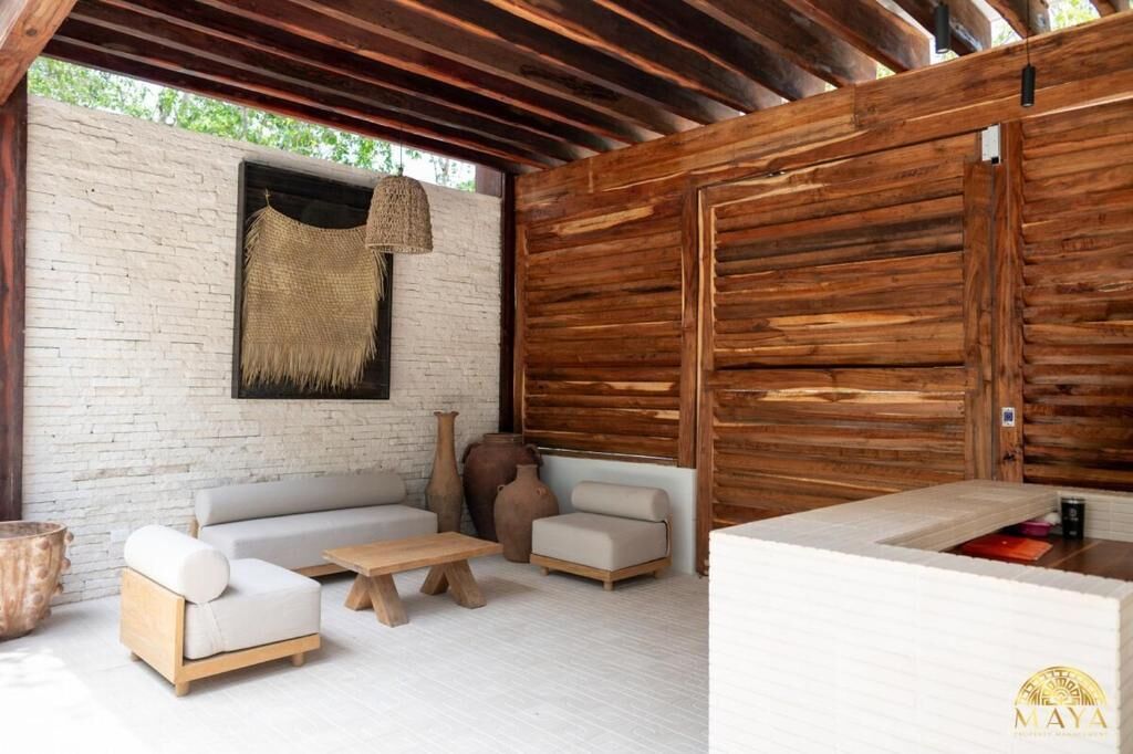 Zona salotto esterna moderna con parete in mattoni bianchi, travi in legno e tessuto intrecciato appeso.