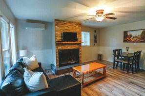 A living room with a fireplace, a television, a ceiling fan, and a dining area with a table and chairs. - Falcon Cottage - 2 Bedroom - Family Friendly (Trent Lakes)