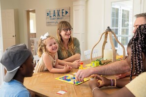 A family playing a board game at a wooden table with a rustic lamp and greenery.