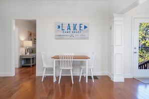 A dining area with a wooden table and two white chairs, a white door, and a wall-mounted sign.