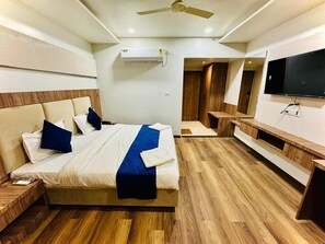 Ett modernt hotellrum med en stor säng, en platt-TV, en takfläkt och ett trägolv.