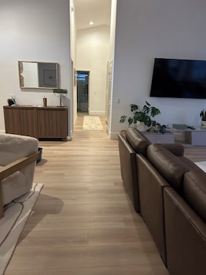 A modern living room with a sofa, a TV mounted on the wall, and a wooden floor. - POOL home newly remodeled with office in beautiful La Quinta (La Quinta)