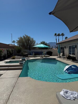 A swimming pool with a patio area, lounge chairs, and a green umbrella. - POOL home newly remodeled with office in beautiful La Quinta (La Quinta)