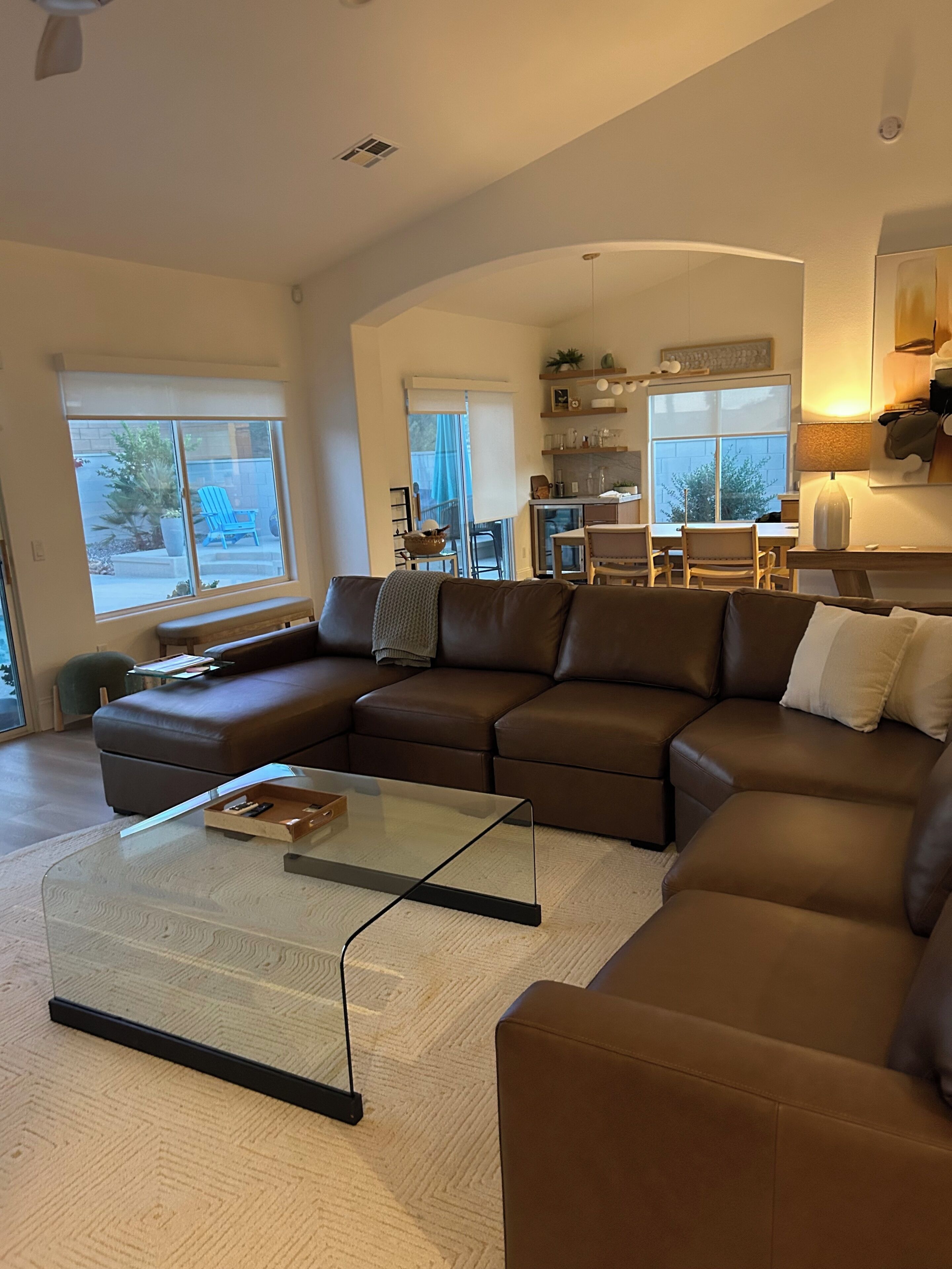 A spacious living room with a large sectional sofa, a glass coffee table, and a dining area with a kitchen in the background.