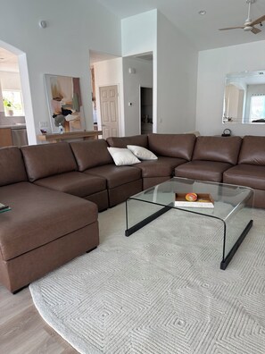 A modern living room with a brown leather sectional sofa, a glass coffee table, and a patterned rug. - POOL home newly remodeled with office in beautiful La Quinta (La Quinta)