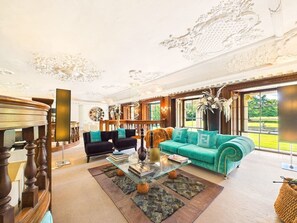A spacious living room with a large teal sofa, a coffee table, and a fireplace. - Umberslade Hall | Luxury Stay | Cinema Room (Hockley Heath)