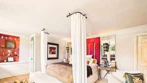 Una camera da letto con un letto a baldacchino, un angolo salotto con un divano, una scrivania e un ampio specchio.