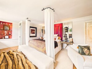 Ein Schlafzimmer mit einem Himmelbett, einer Sitzecke mit einer Couch, einem Schreibtisch und einem großen Spiegel.