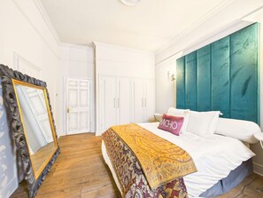 Een slaapkamer met een bed, een spiegel, een kast en een turquoise hoofdeinde.