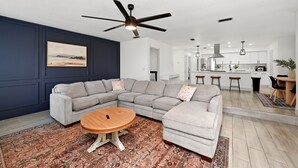 A modern living room with a sectional sofa, a round coffee table, and a ceiling fan. - Country Retreat home with Private pool,Near Orlando International Airport (Kissimmee)