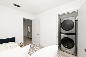 A bedroom with a bed, a washing machine, and a door leading to a bathroom. - Country Retreat home with Private pool,Near Orlando International Airport (Kissimmee)